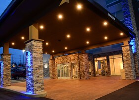 Entrada de hotel con fachada de piedra, puertas de vidrio y un área techada con luces.