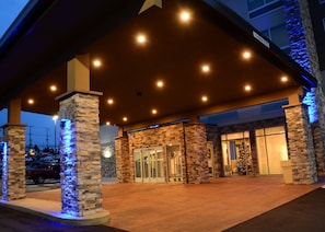A hotel entrance with a stone facade, glass doors, and a covered area with lights.
