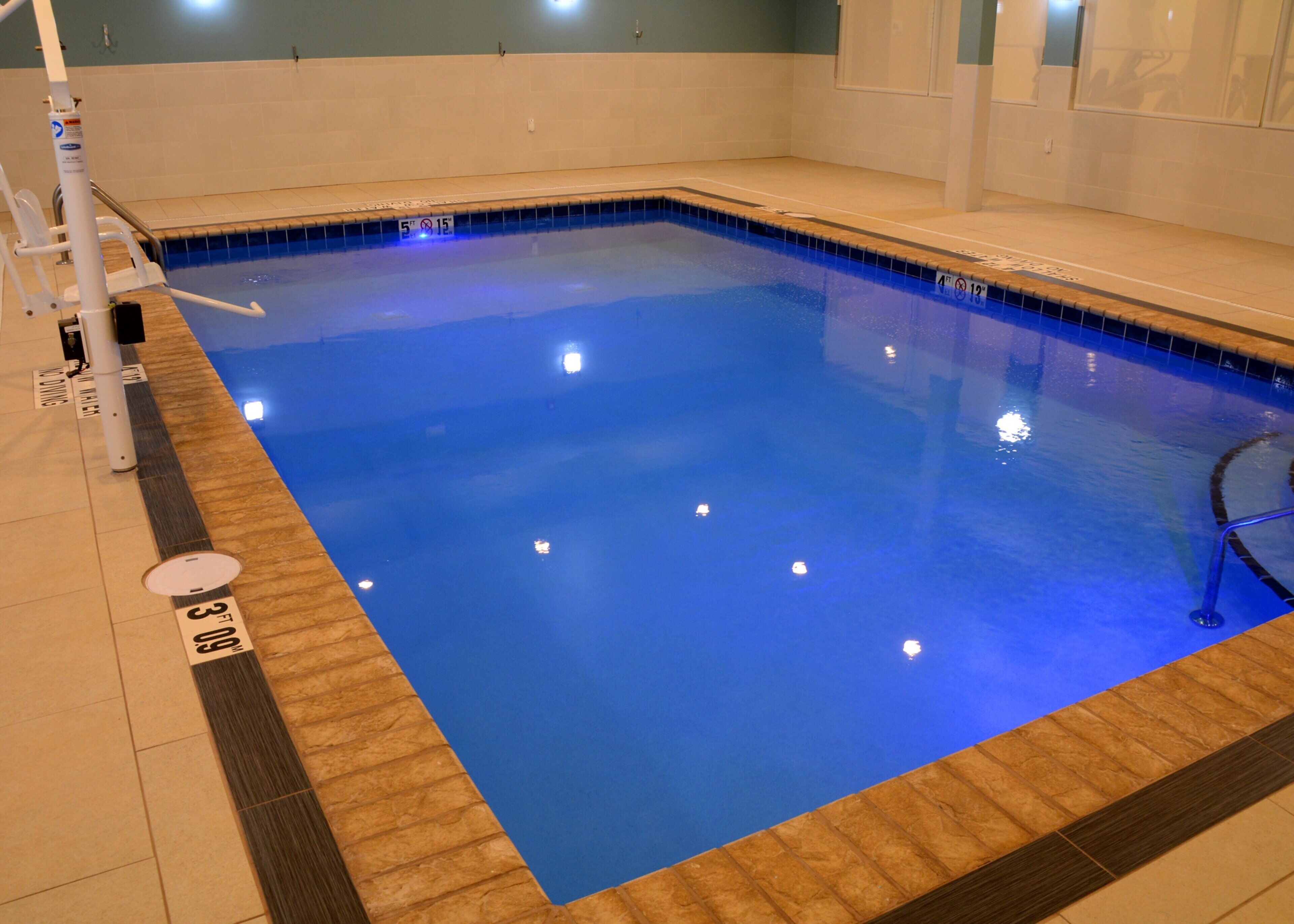 Une piscine à l’eau d’un bleu cristallin, avec une terrasse en bois et un sol carrelé.
