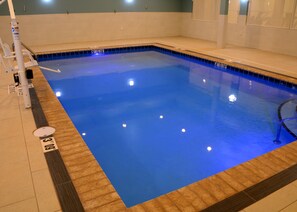 Piscina com água azul cristalina, deck de madeira e piso de azulejo.