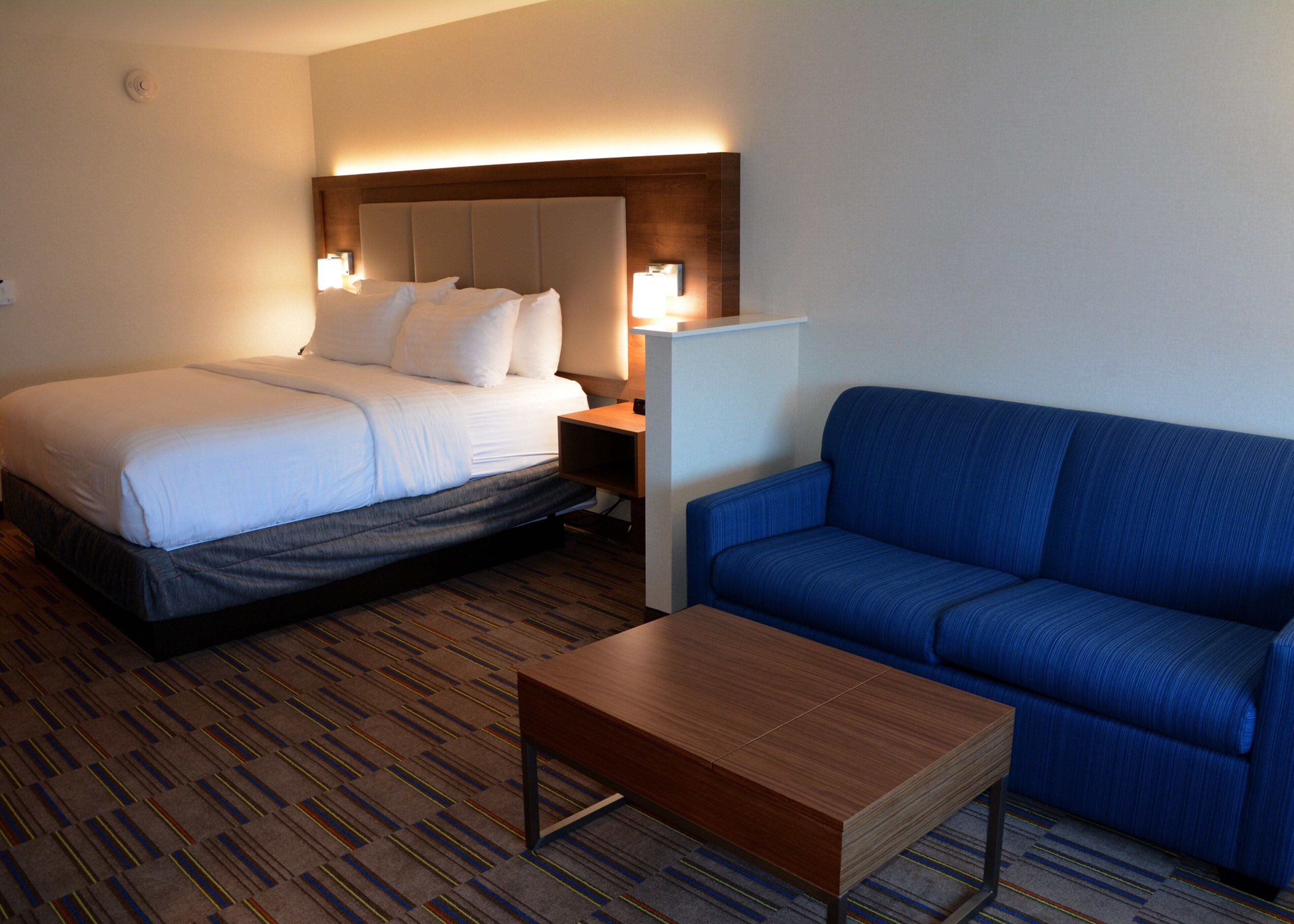 Una habitación de hotel con una cama, un sofá azul y una mesa de centro de madera.