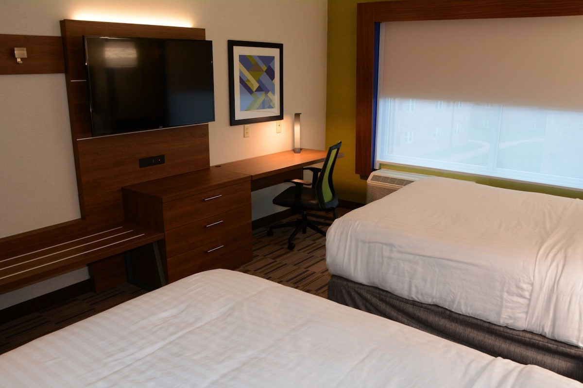 A hotel room with two beds, a desk with a chair, a television, and a framed picture on the wall.