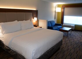 Habitación de hotel con una cama grande, un escritorio, una silla, una lámpara y una ventana con aire acondicionado.