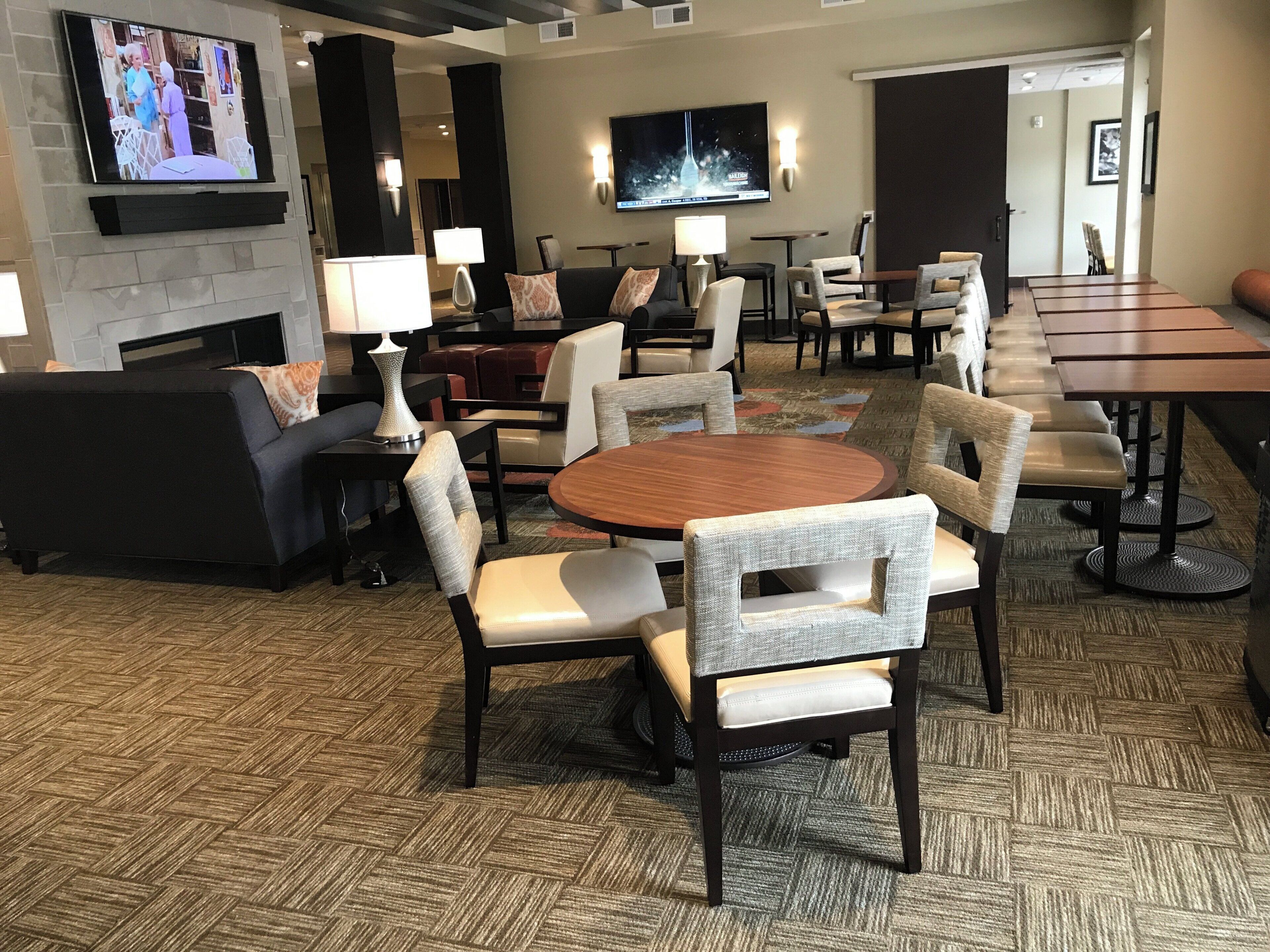 Un hall d’hôtel doté d’une cheminée, de canapés, de tables à manger et d’un écran de télévision.