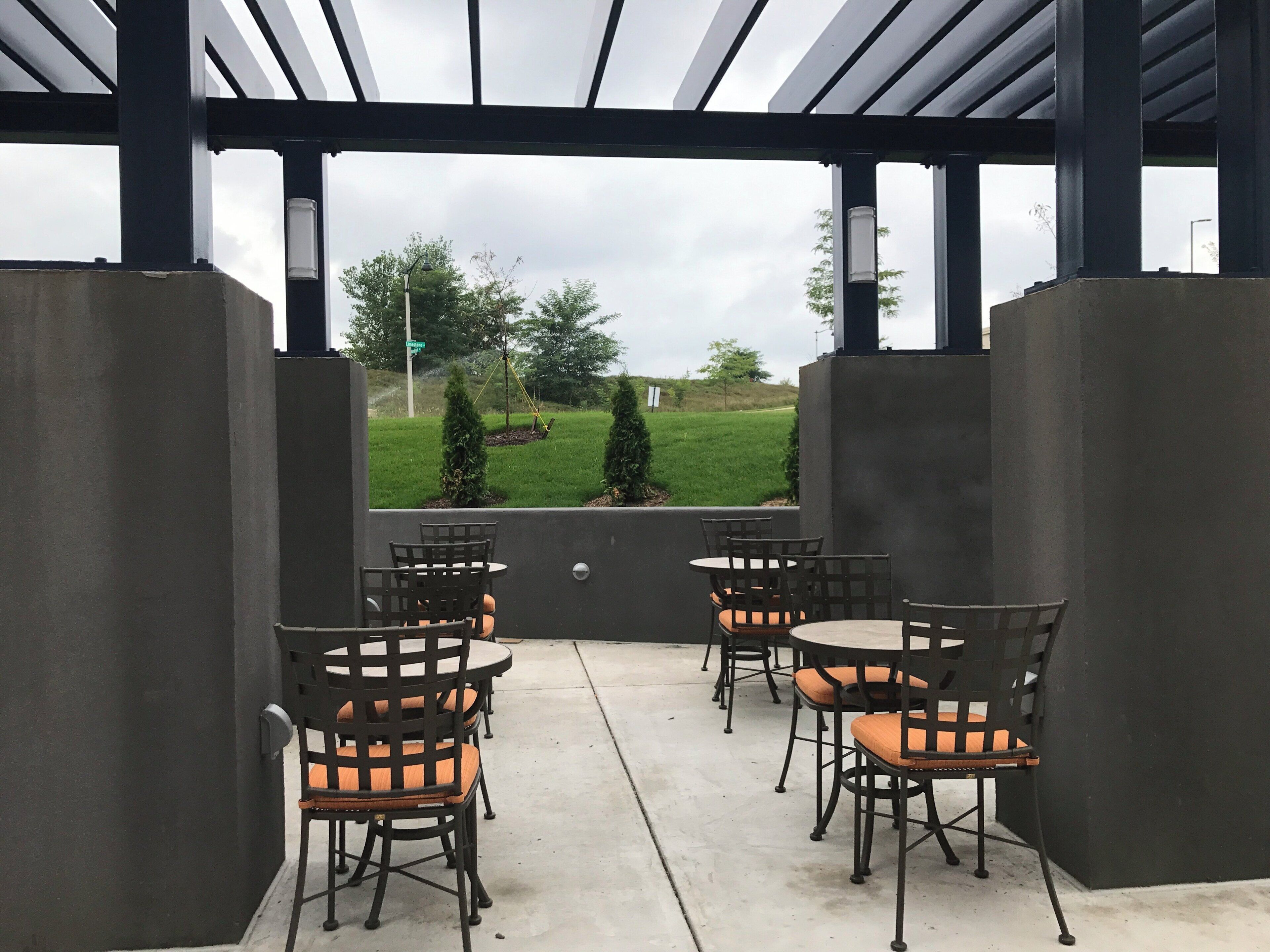 An outdoor patio with four tables and chairs, a concrete floor, and a view of a grassy area with trees.