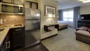 Una habitación de hotel moderna con kitchenette, una cama, un televisor y un sofá.