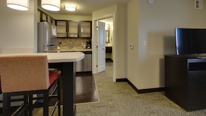 Una cocina moderna con una isla central, una zona de comedor con una silla y un televisor sobre un mueble.