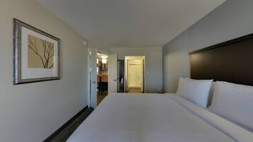 A hotel room with a large bed, a framed picture on the wall, and a view of the bathroom and kitchen through an open door.
