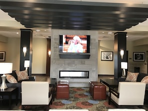 A modern lobby with a fireplace, comfortable seating, and a flat-screen TV mounted above it. - Staybridge Suites Madison - Fitchburg by IHG (Madison)