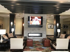 A modern lobby with a fireplace, comfortable seating, and a flat-screen TV mounted above it.