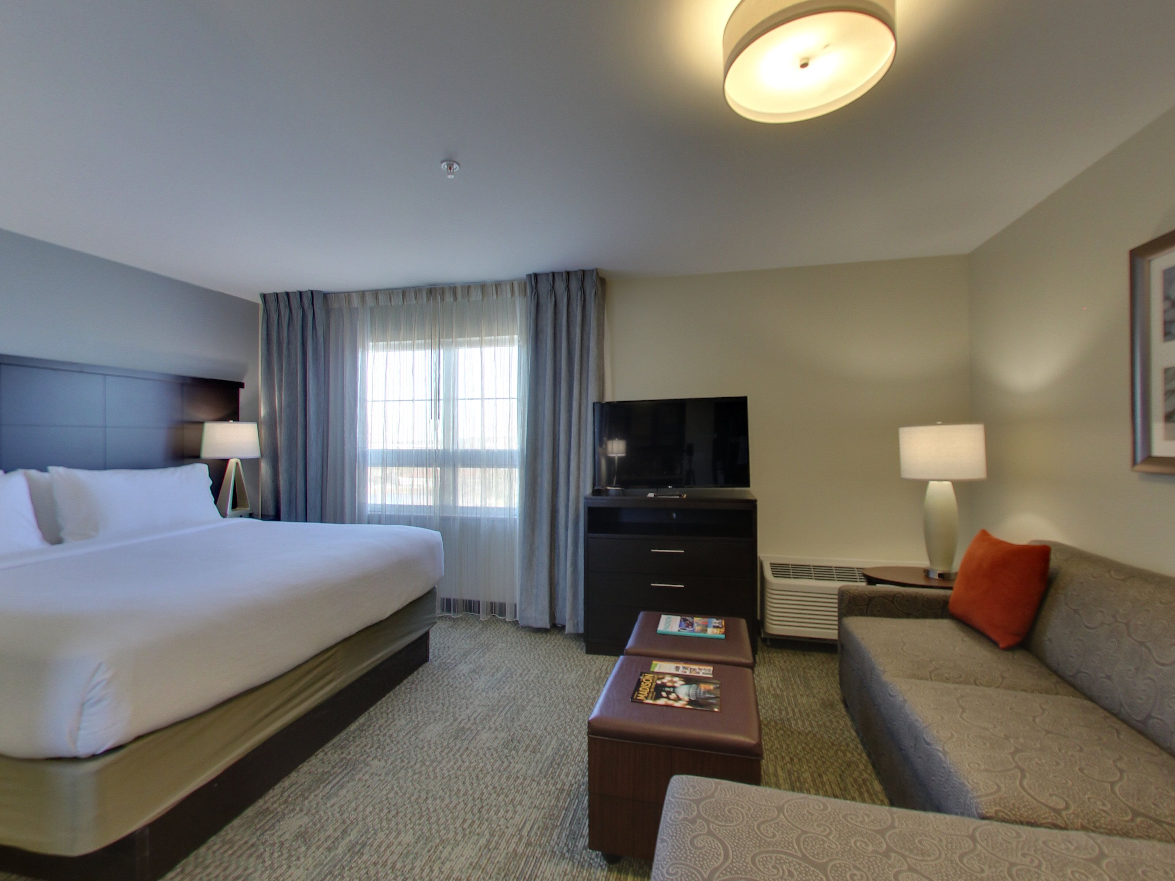 A hotel room with a large bed, a flat-screen TV, a sofa, a coffee table, and a window with curtains.