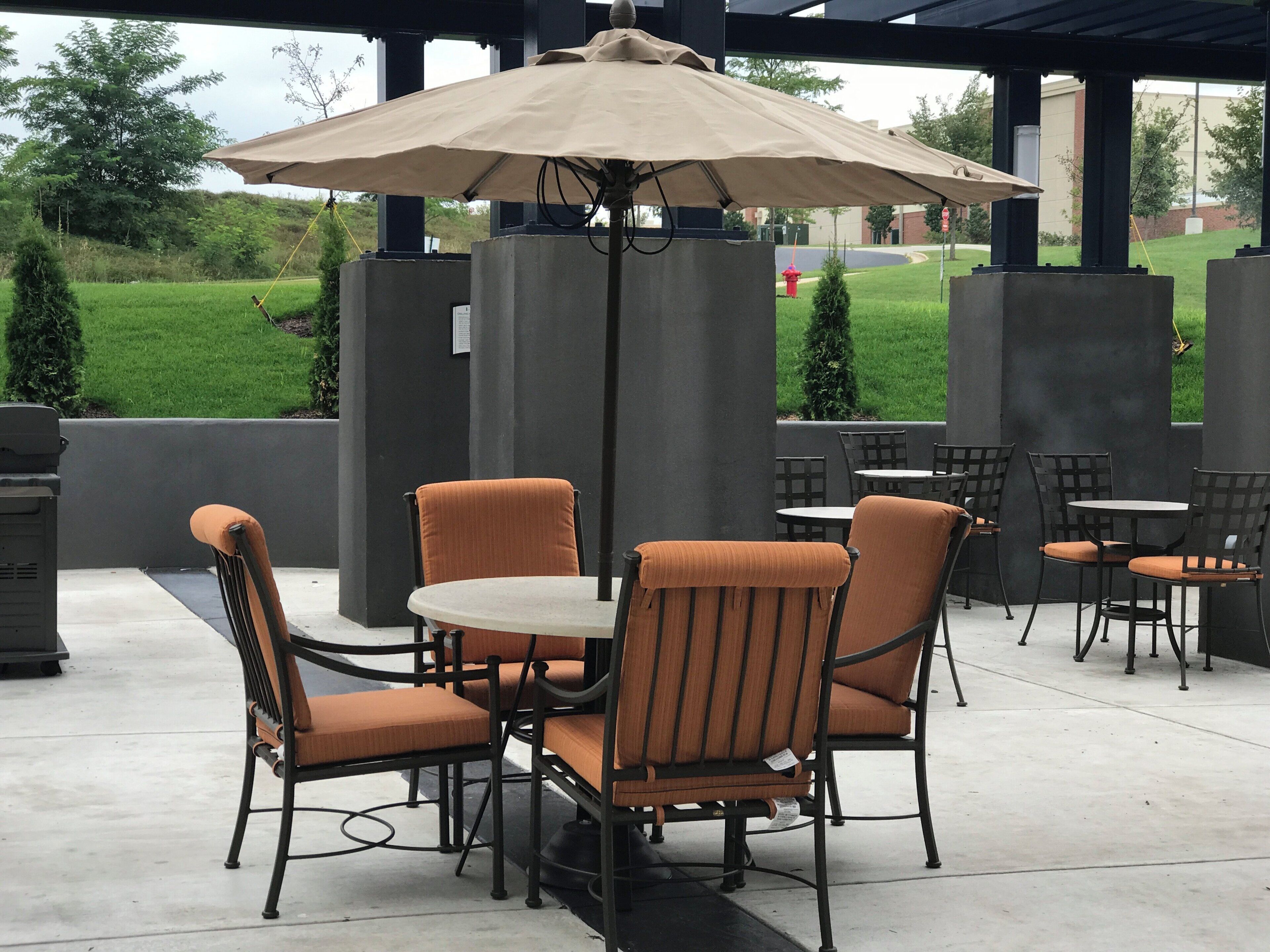 An outdoor patio area with tables and chairs, a covered seating area, and a view of a green landscape.