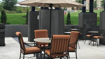 An outdoor patio area with tables and chairs, a covered seating area, and a view of a green landscape.