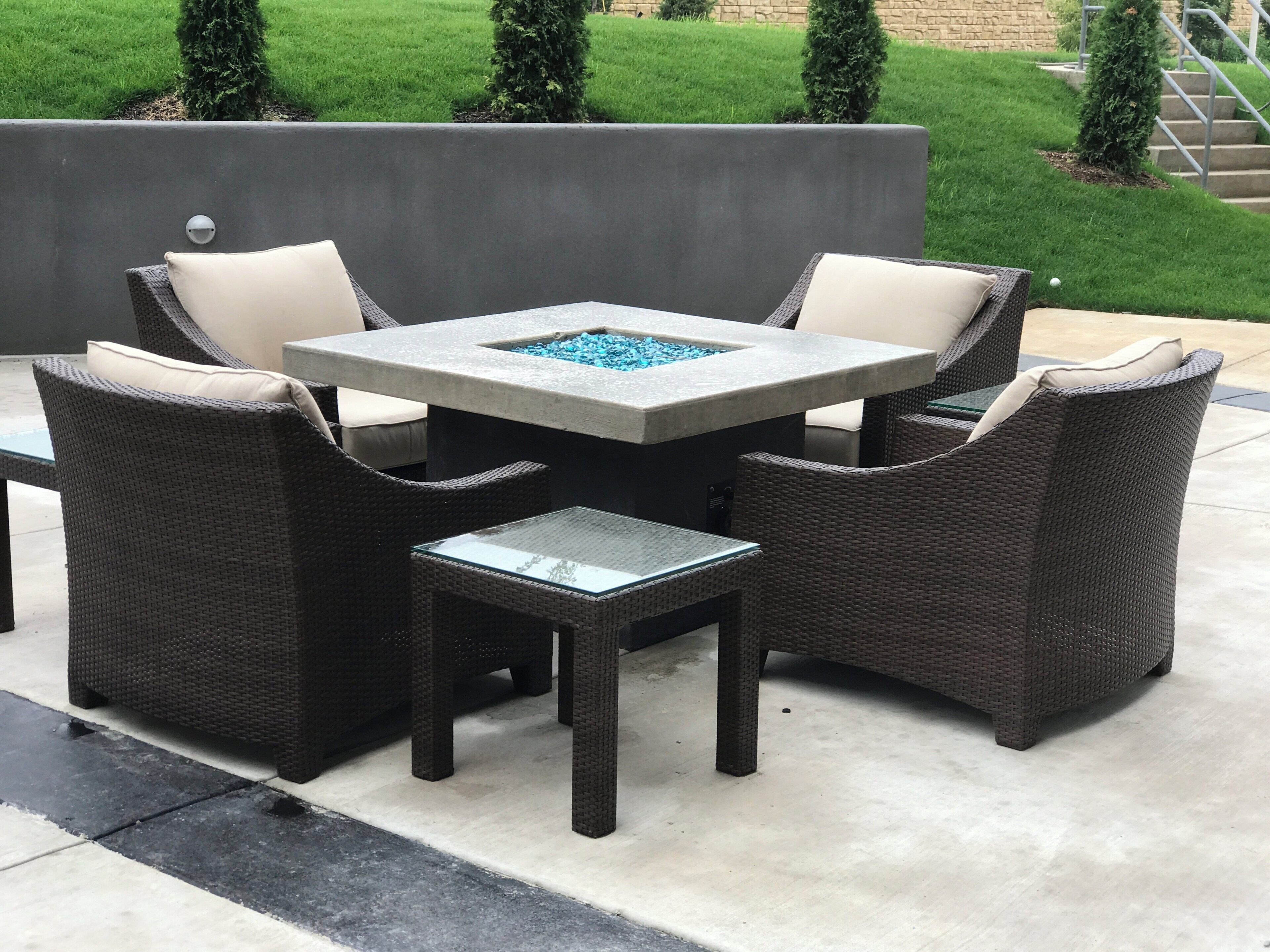 A patio area with a square table and four chairs, a small fire feature, and a stone wall in the background.