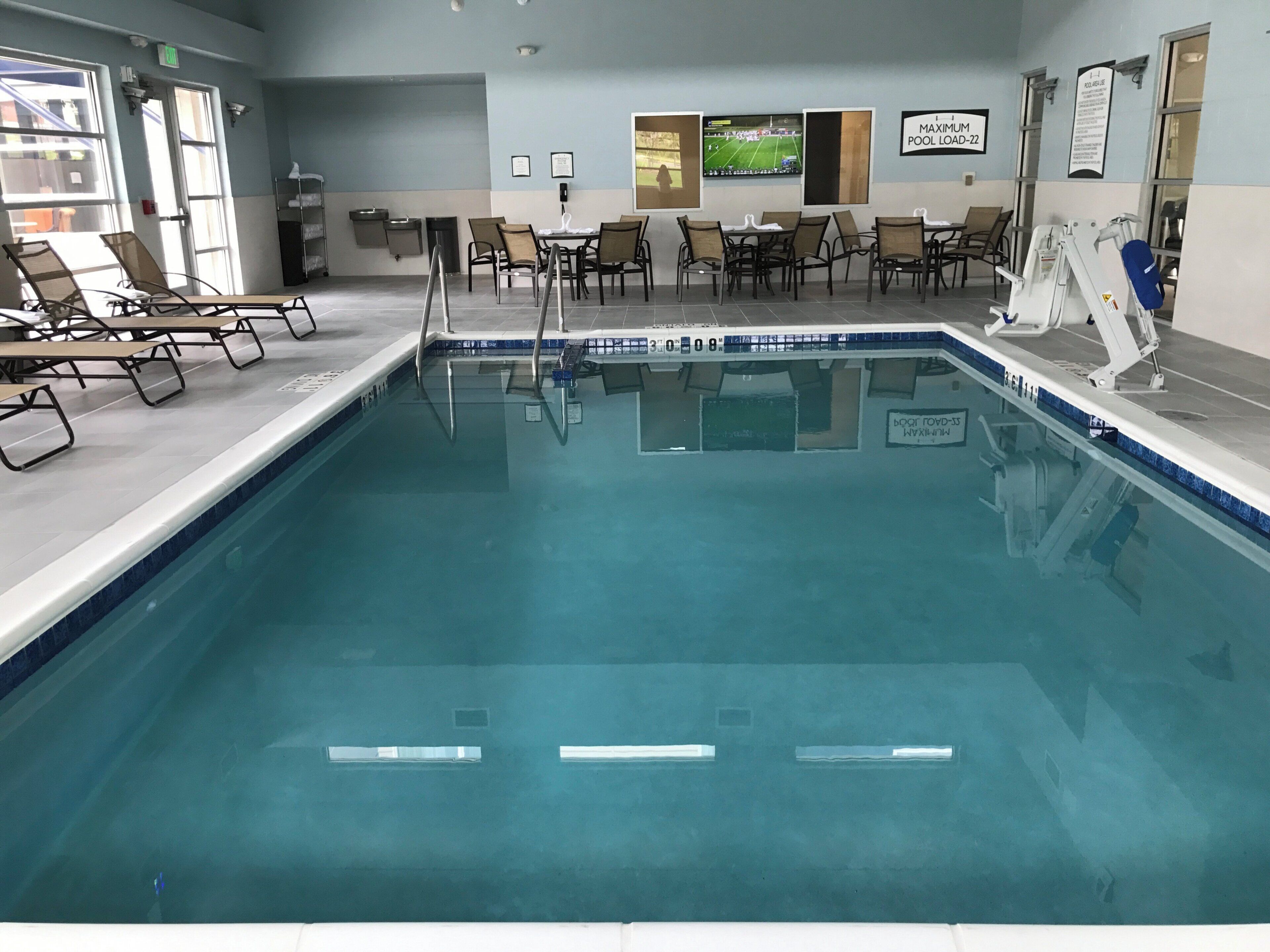 Une piscine intérieure dotée d’un plongeoir, de chaises longues et d’un espace aménagé au bord de la piscine offrant une vue sur l’extérieur.