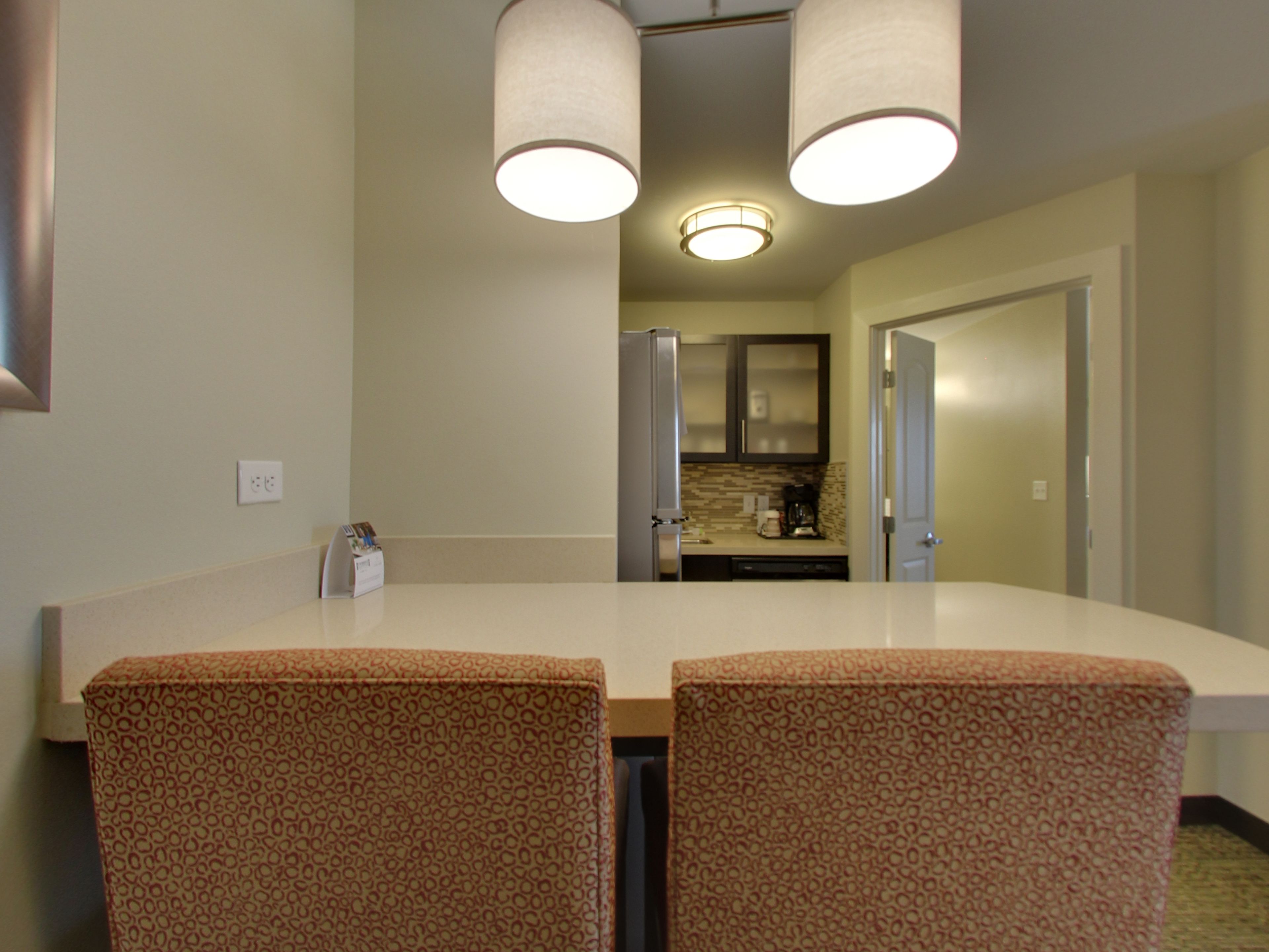 Un comedor con una mesa blanca y sillas estampadas, una cocina al fondo y una puerta que da a otra habitación.