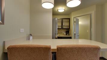 Un comedor con una mesa blanca y sillas estampadas, una cocina al fondo y una puerta que da a otra habitación.