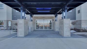 A modern building entrance with a covered walkway, glass doors, and a parking area with designated spaces.