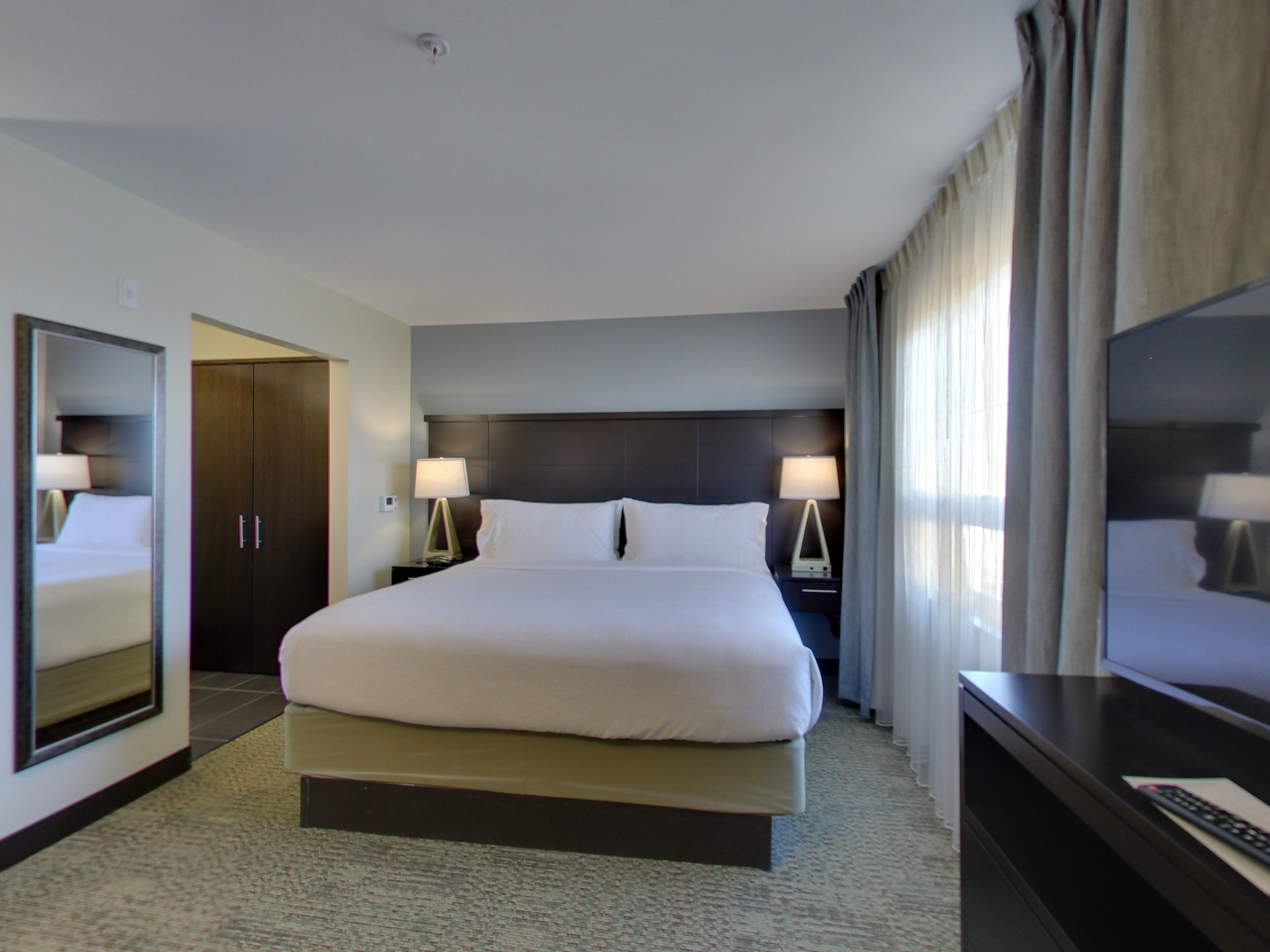A hotel room with a large bed, two bedside tables with lamps, a wardrobe, and a television on a stand.