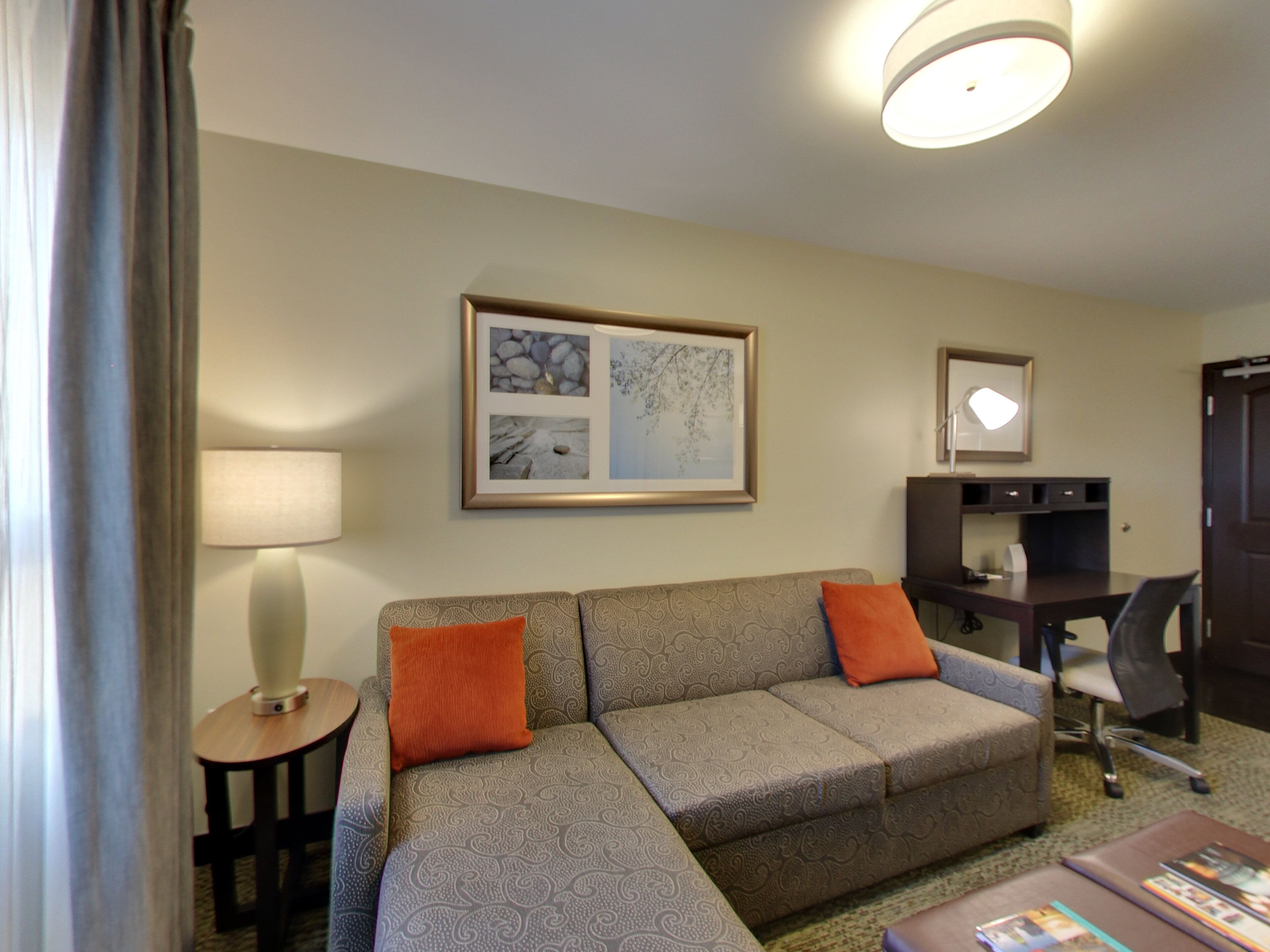 A hotel room with a sofa, a desk, a lamp, and a framed picture on the wall.