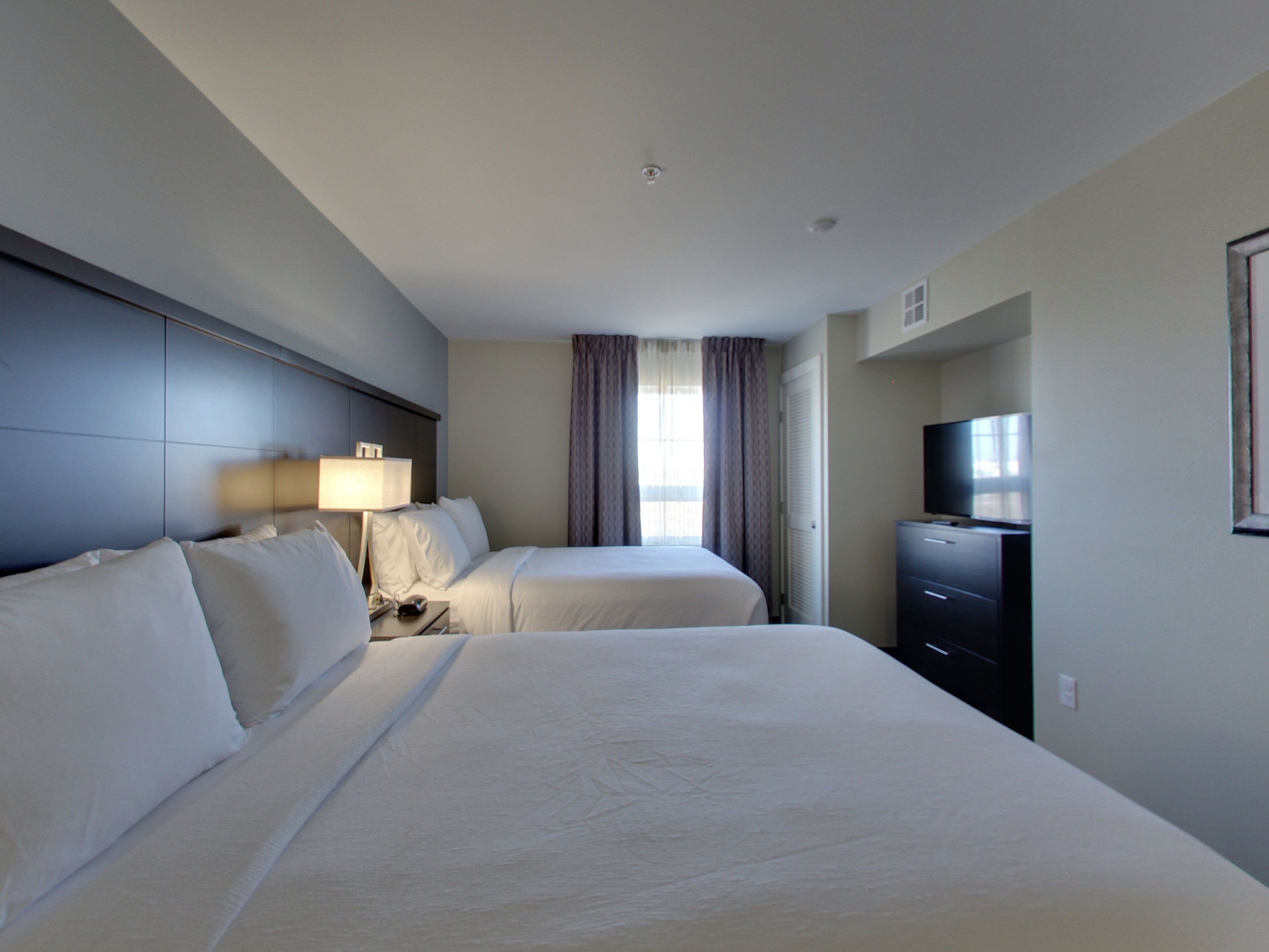 A hotel room with two beds, a desk, a television, and a window with curtains.