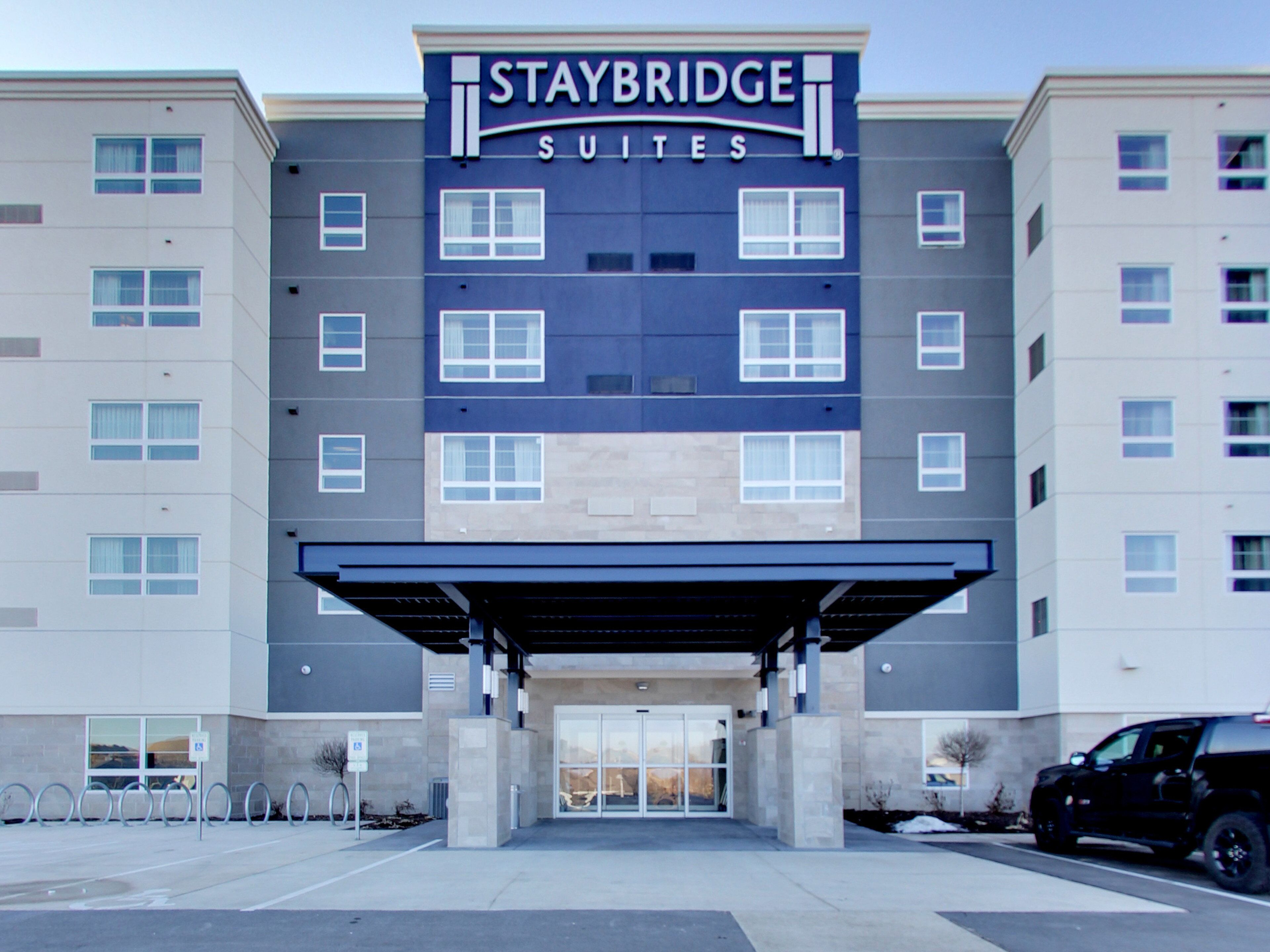 A Staybridge Suites hotel building with a covered entrance, multiple windows, and a parking area.