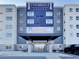 A Staybridge Suites hotel building with a covered entrance, multiple windows, and a parking area.