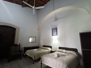 A room with two beds, a ceiling fan, a small table, and a chair.