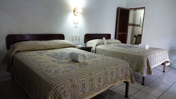 A hotel room with two beds, each with a patterned bedspread, a nightstand, a wall-mounted light, and a mirror.