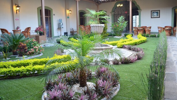 A courtyard with a fountain, lush greenery, and outdoor seating. - La Merced Hotel (Colima)