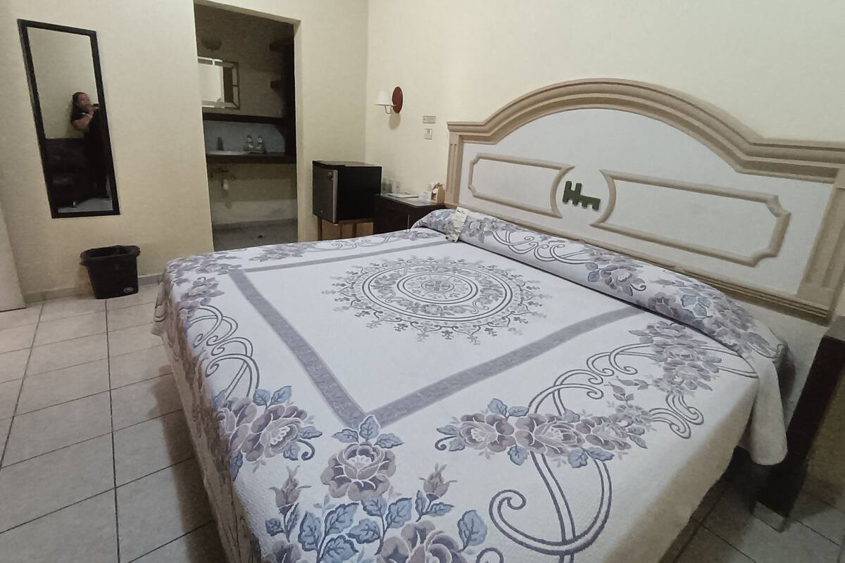 A bedroom with a bed, a mirror, a dresser, and a door leading to a bathroom.