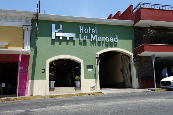 Hotel La Merced with a green facade, two arched entrances, and a visible parking area.