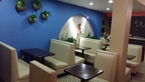 A seating area with cushioned chairs and tables, a decorative wall with plants, and a statue. - La Merced Hotel (Colima)