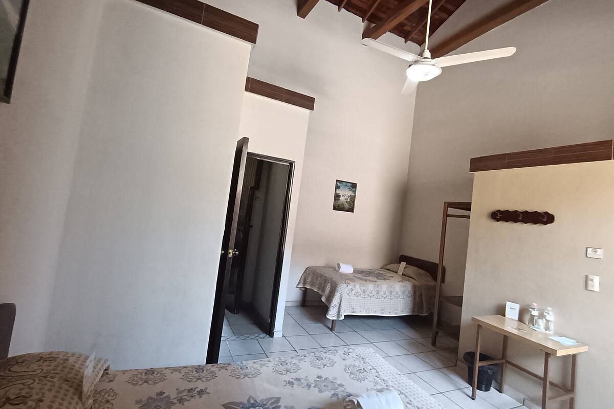 A narrow hallway with a bed on the right, a small table with items, and a ceiling fan.