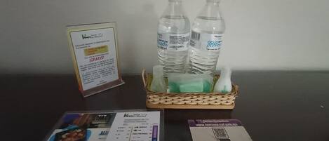 Una mesa con un menú, un código QR para servicios del hotel y una cesta con botellas de agua y una botella verde.