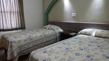 A hotel room with two beds, each with floral-patterned bedding, a wooden headboard, and a green arch over the window.