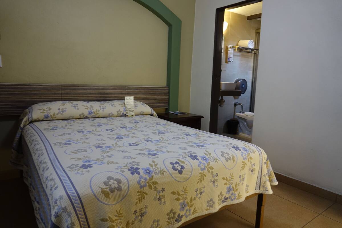A hotel room with a bed, a nightstand, and a bathroom visible through an open door.