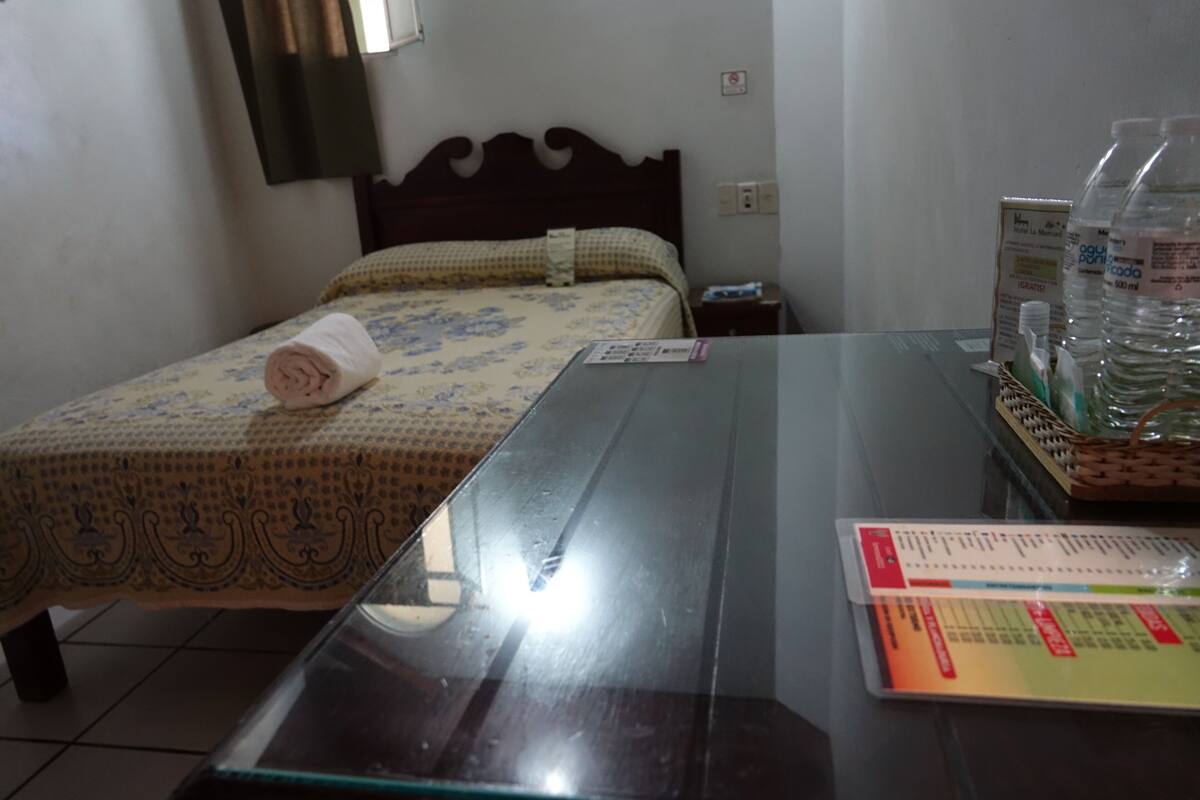 A hotel room with a bed, a glass-top table, and a tray with bottled water and toiletries.