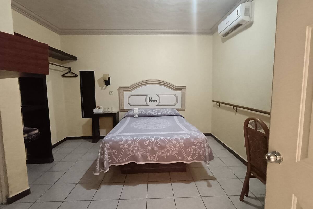 A bedroom with a bed, a nightstand, an air conditioning unit, and a door.
