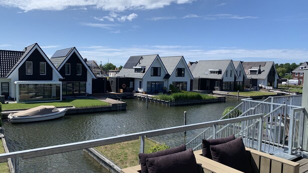 Vista del río con una hilera de casas modernas, un muelle y un bote.
