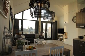 Relax in this spacious living area with a sofa near a window offering a view of the outdoors, a dining table, and a kitchen with an oven.