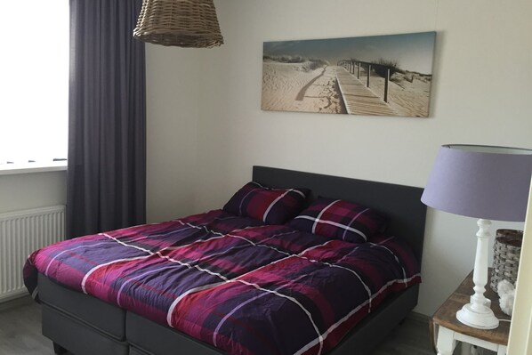Ein Schlafzimmer mit Bett, einem Wandbild, einer Lampe und einem Fenster mit Vorhängen.