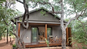 Una cabaña con terraza de madera, amplios ventanales correderas y un área de estar con mesa y sillas.