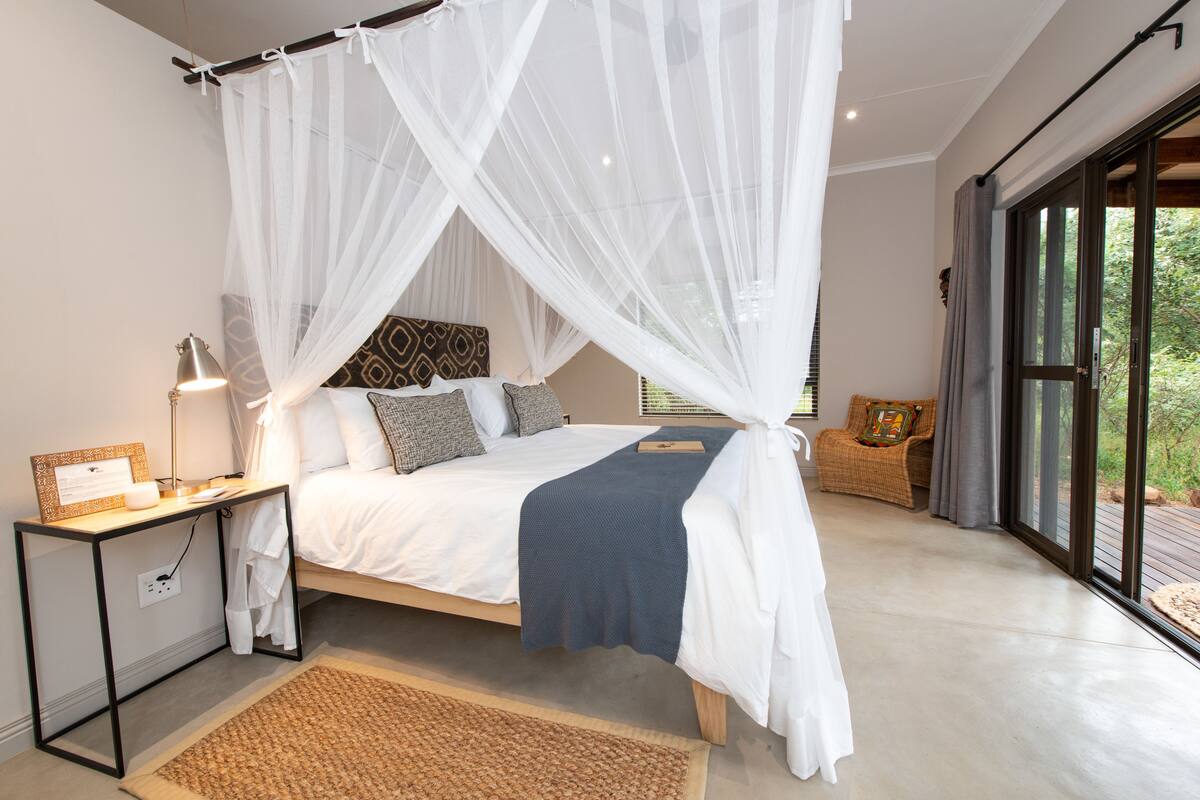 A bedroom with a canopy bed, bedside table, and a view of the outdoors.
