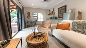 Una sala moderna con un sofá, un reposapiés de mimbre y un comedor con sillas y una mesa.