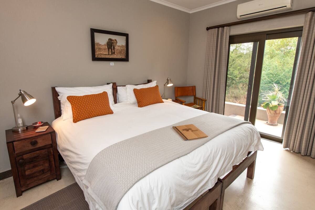 A neatly made bed with white and orange bedding, a bedside table with a lamp, and a framed picture on the wall.