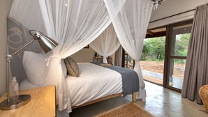 Un dormitorio con cama, lámpara de noche, mesita de noche y cortinas traslúcidas.