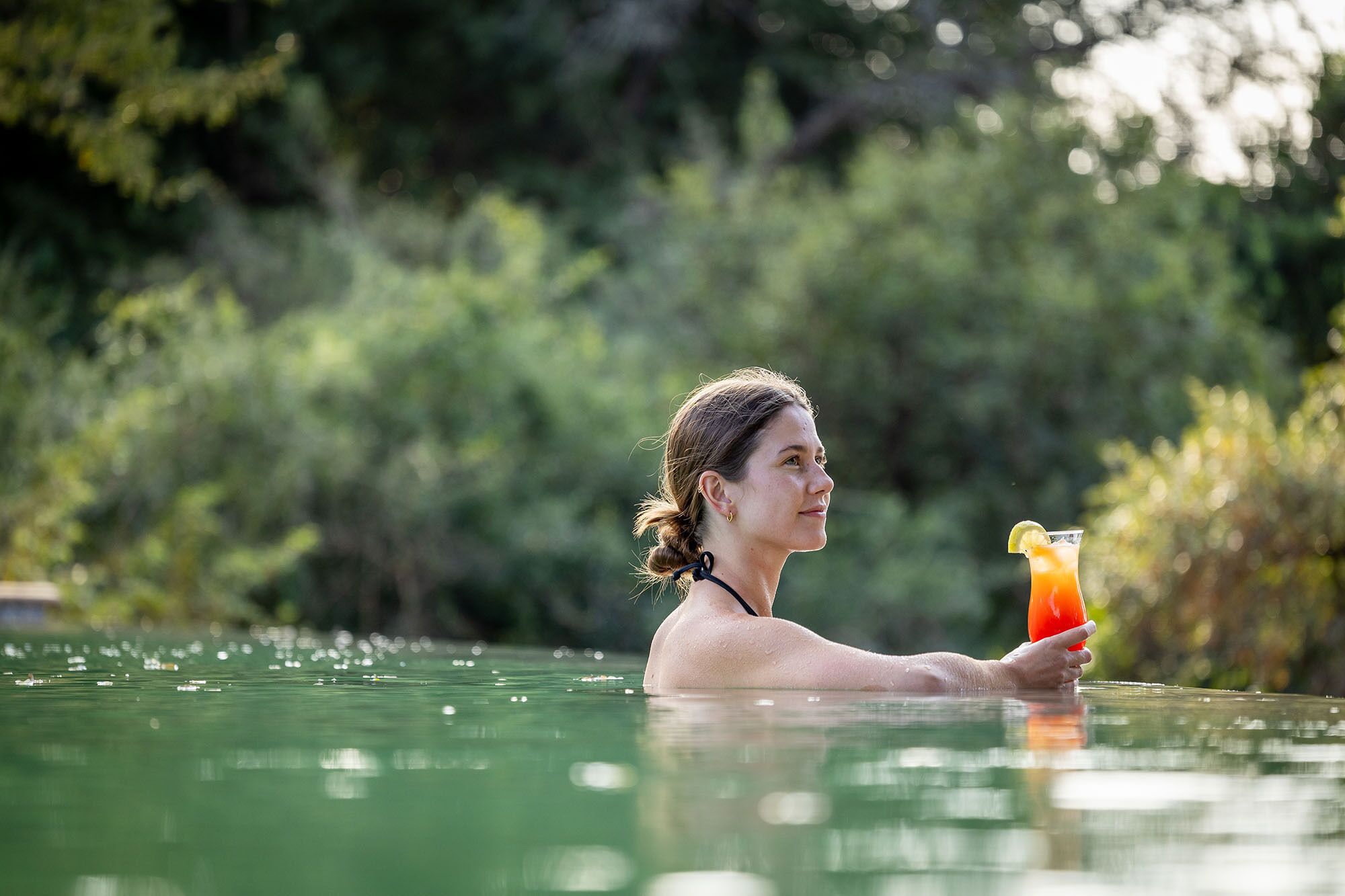 A person in a swimming pool holding a drink with a lime wedge.