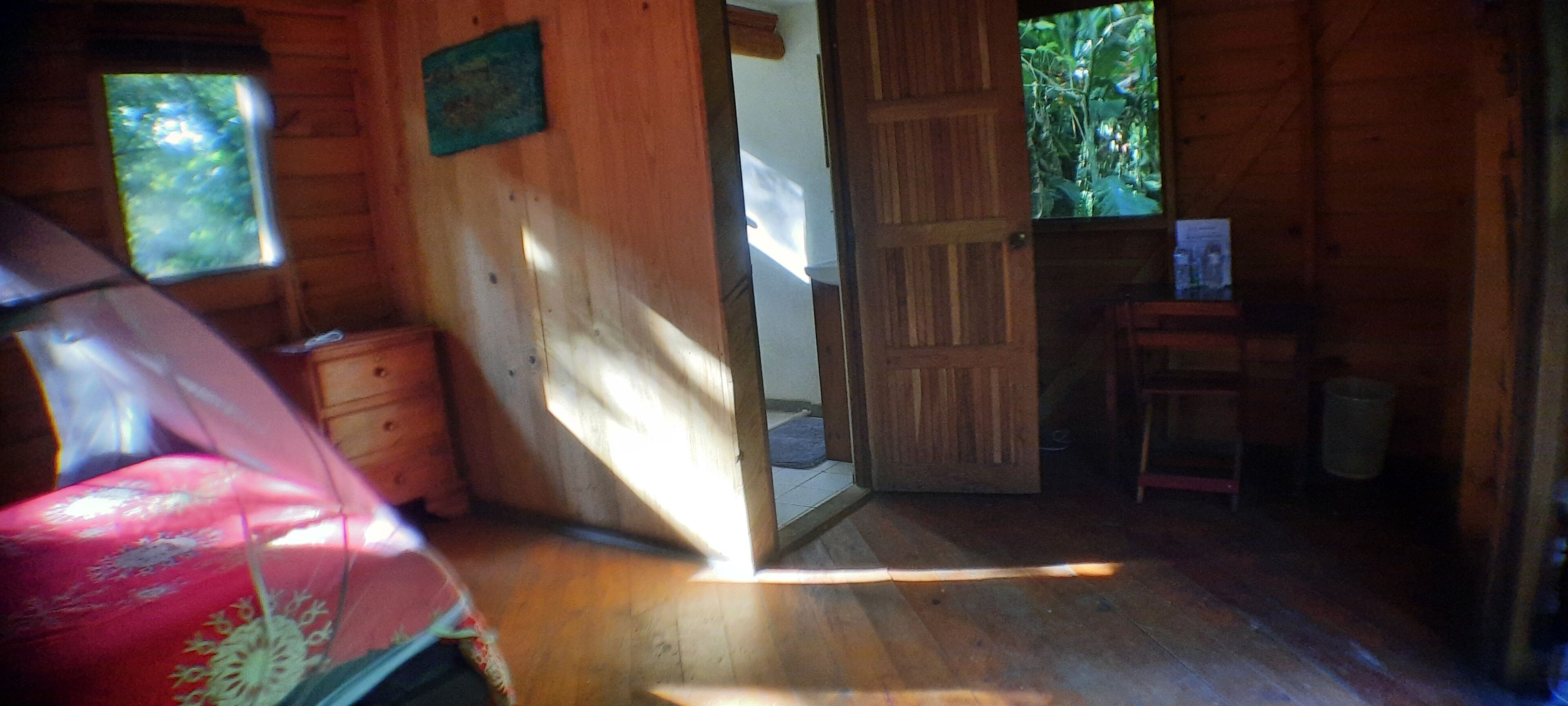 Interno di una baita in legno con una porta in legno che dà su un balcone, un tavolino e una sedia.