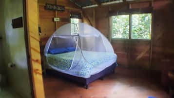Une petite pièce agréable, avec un lit recouvert d’une moustiquaire, une fenêtre donnant sur les arbres et un plancher en bois.